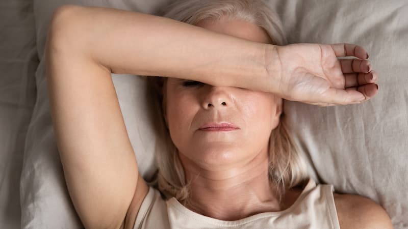 woman laying on a pillow with hand over her face during menopause fatigue