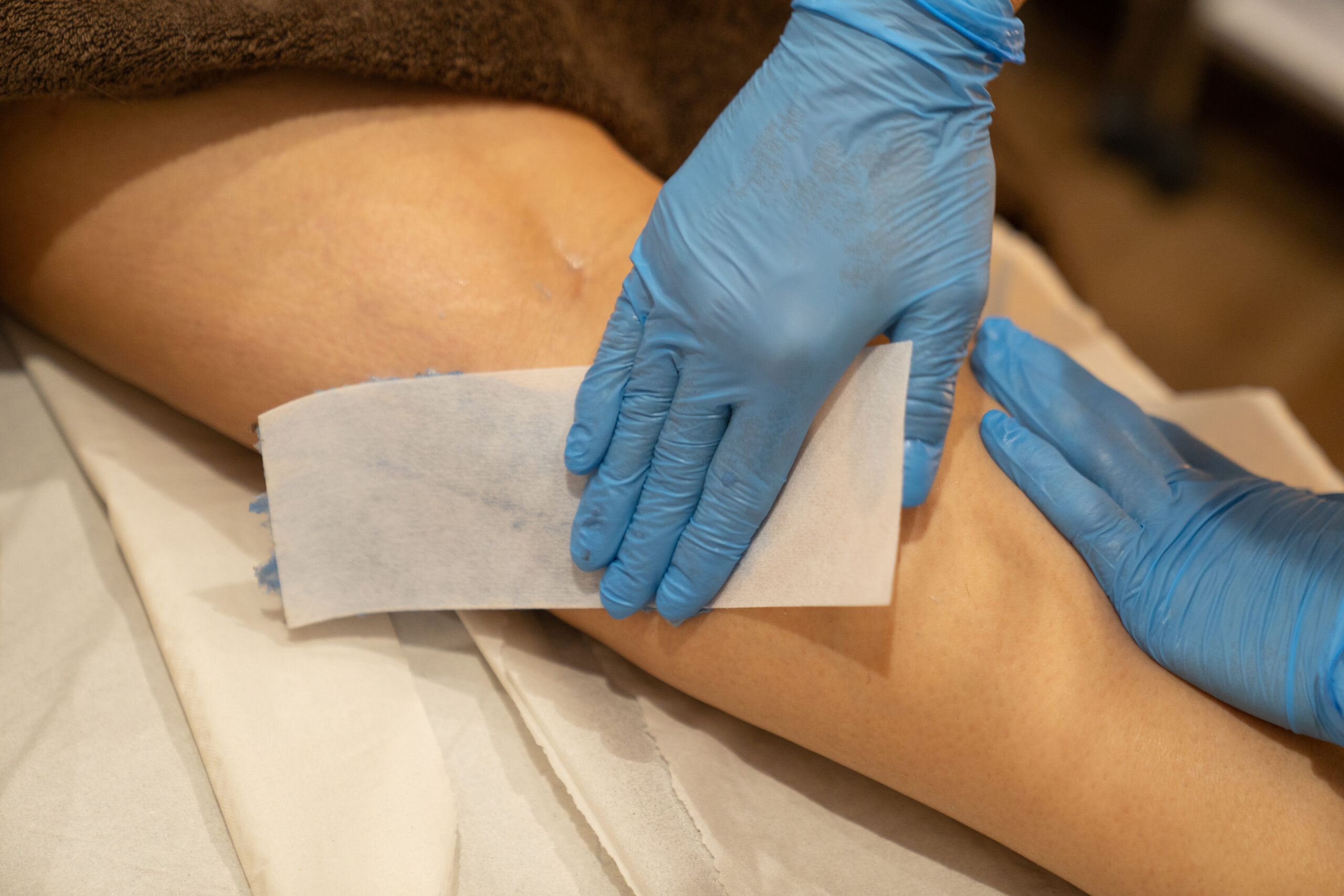 Male waxing treatment being applied to leg with blue gloves in professional salon
